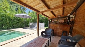 Ein überdachter Außenbereich mit Pool, Liegestühlen und Bar.