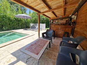 Ein überdachter Außenbereich mit Pool, Liegestühlen und Bar.