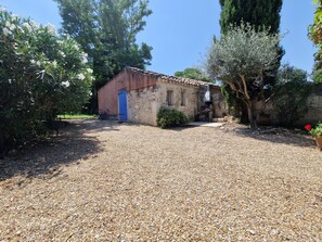 Un edificio rustico con una porta blu, immerso tra ghiaia e alberi.