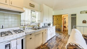 A kitchen with a stove, sink, and microwave, a wooden floor, and a door leading to another room. - Deck & Mtn Views! Woodsy Haven in Running Springs (Running Springs)