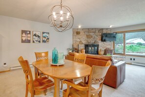 A dining area with a wooden table and chairs, a stone fireplace, and a television mounted on the wall. - Keystone Lakefront Retreat! Pool & Hot Tub Access (Keystone)