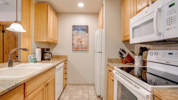 A kitchen with wooden cabinets, a white refrigerator, a microwave, an oven, and a sink. - Keystone Lakefront Retreat! Pool & Hot Tub Access (Keystone)