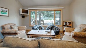 A living room with a large window, a flat-screen TV mounted on the wall, and a bookshelf. - Keystone Lakefront Retreat! Pool & Hot Tub Access (Keystone)