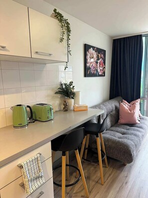 Eine moderne Küche mit Arbeitsplatte, Wasserkocher, Toaster und einer Pflanze. Ein Sofa mit Kissen und ein Gemälde an der Wand.