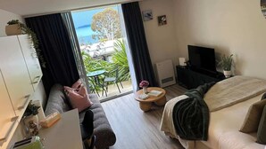 Ett modernt hotellrum med ett stort fönster, en soffa, en säng, en tv och ett litet bord.