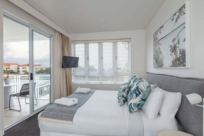 Ett hotellrum med en säng, en tv, en balkong med en stol och en tavla på väggen.