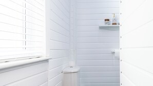 Een kleine badkamer met witte wanden, een toilet, een raam en een plank met toiletartikelen.
