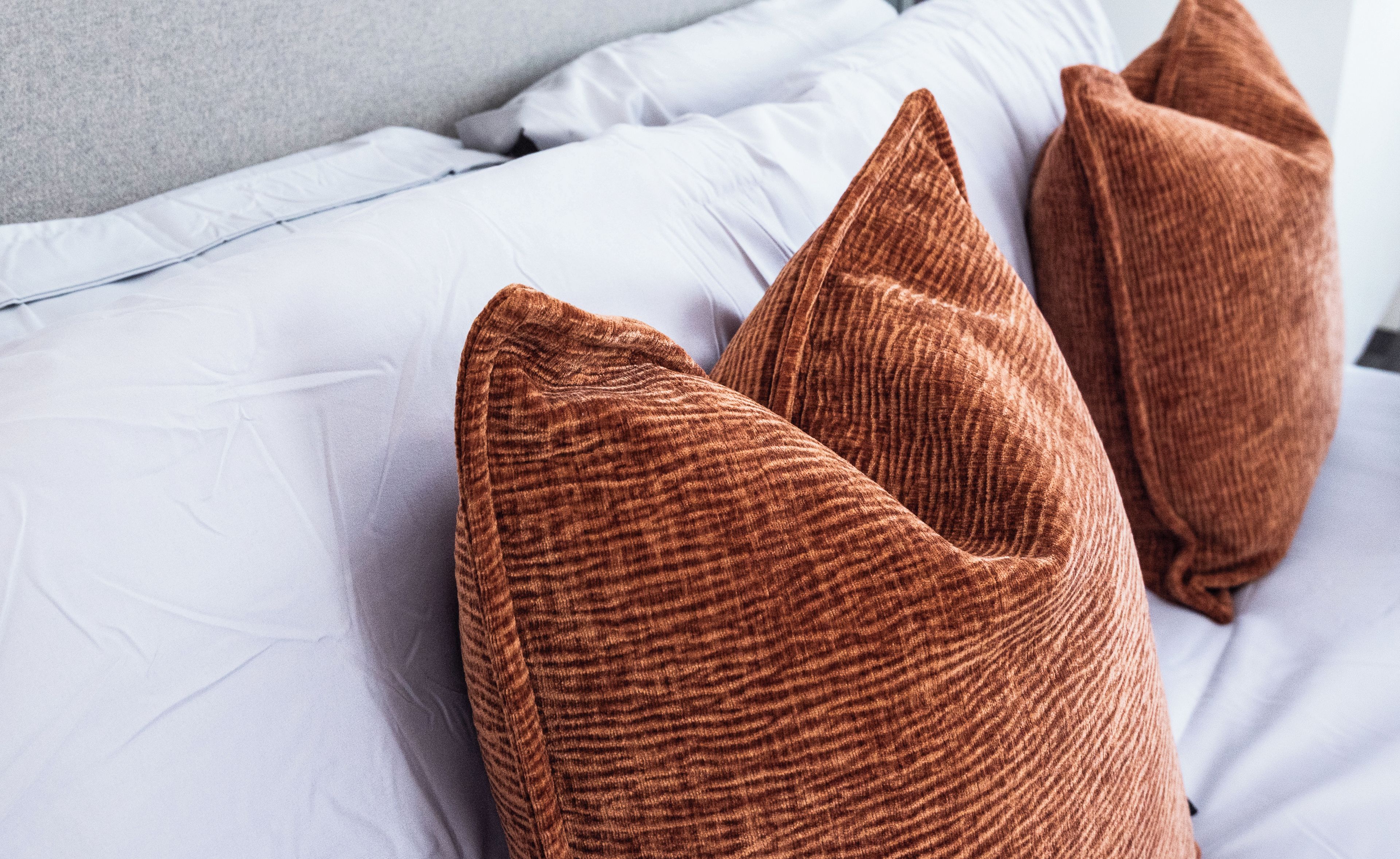 Una cama con ropa de cama blanca y almohadas marrones.