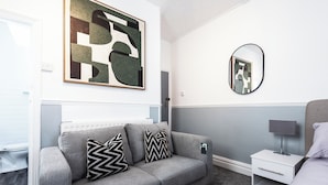 Een moderne slaapkamer met een grijze bank, een nachtkastje, een lamp en abstracte kunst aan de muur.