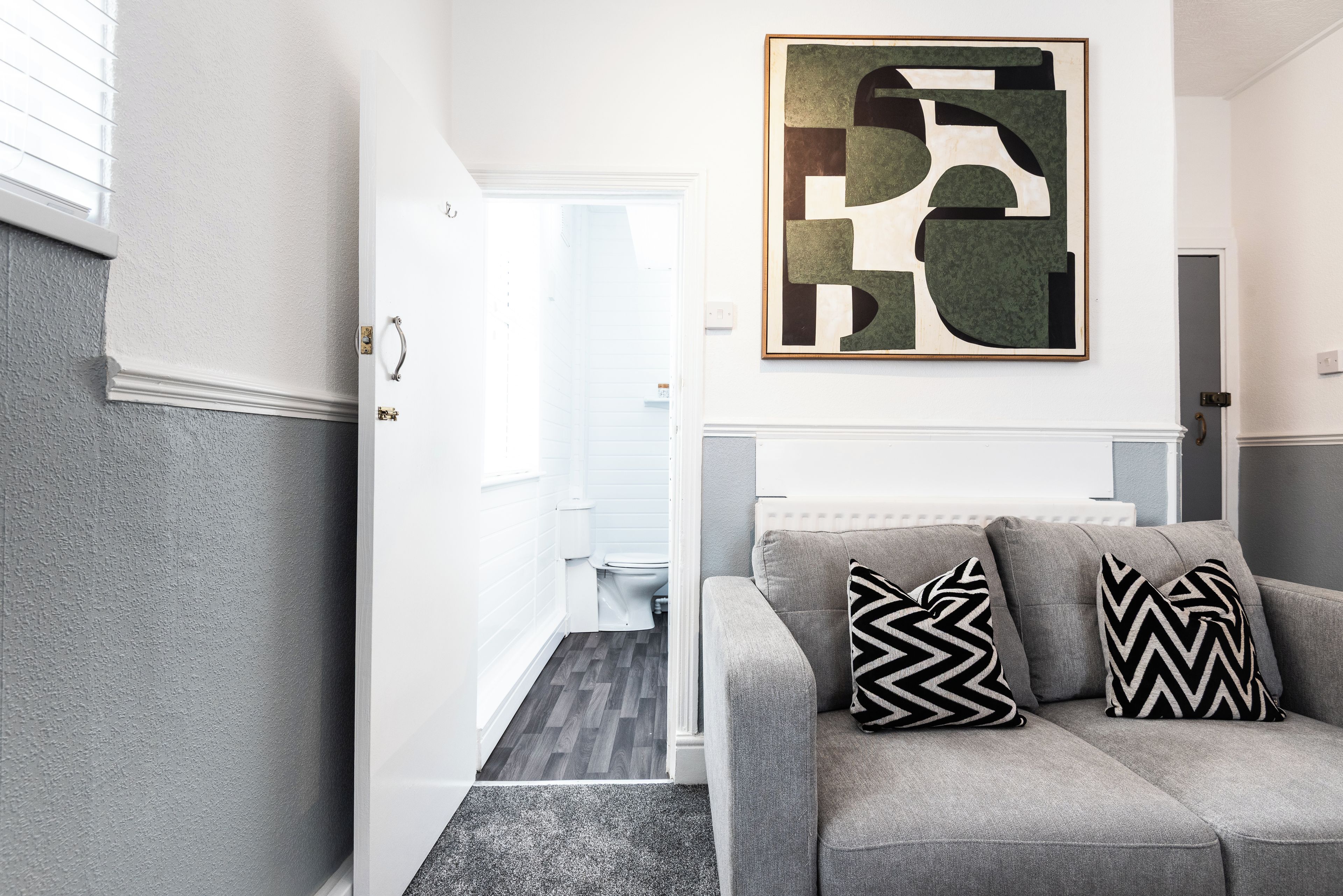 Ein modernes Wohnzimmer mit einem grauen Sofa, zwei gemusterten Kissen und einem modernen, abstrakten Gemälde an der Wand.