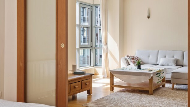A well-lit room with a bed, a sofa, a coffee table, and a view of the outside through a window.