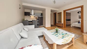 A modern living room with a white sofa, a wooden coffee table, and a kitchen in the background.