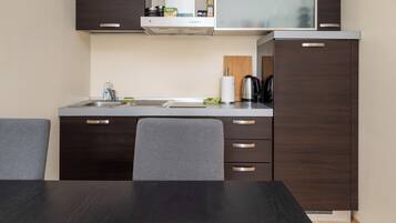 A compact kitchen with a sink, stove, and cabinets. There is a dining table with chairs.