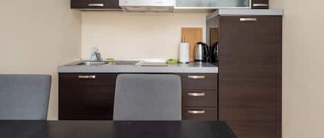 Cocina compacta con lavamanos, estufa y armarios. Hay una mesa de comedor con sillas.
