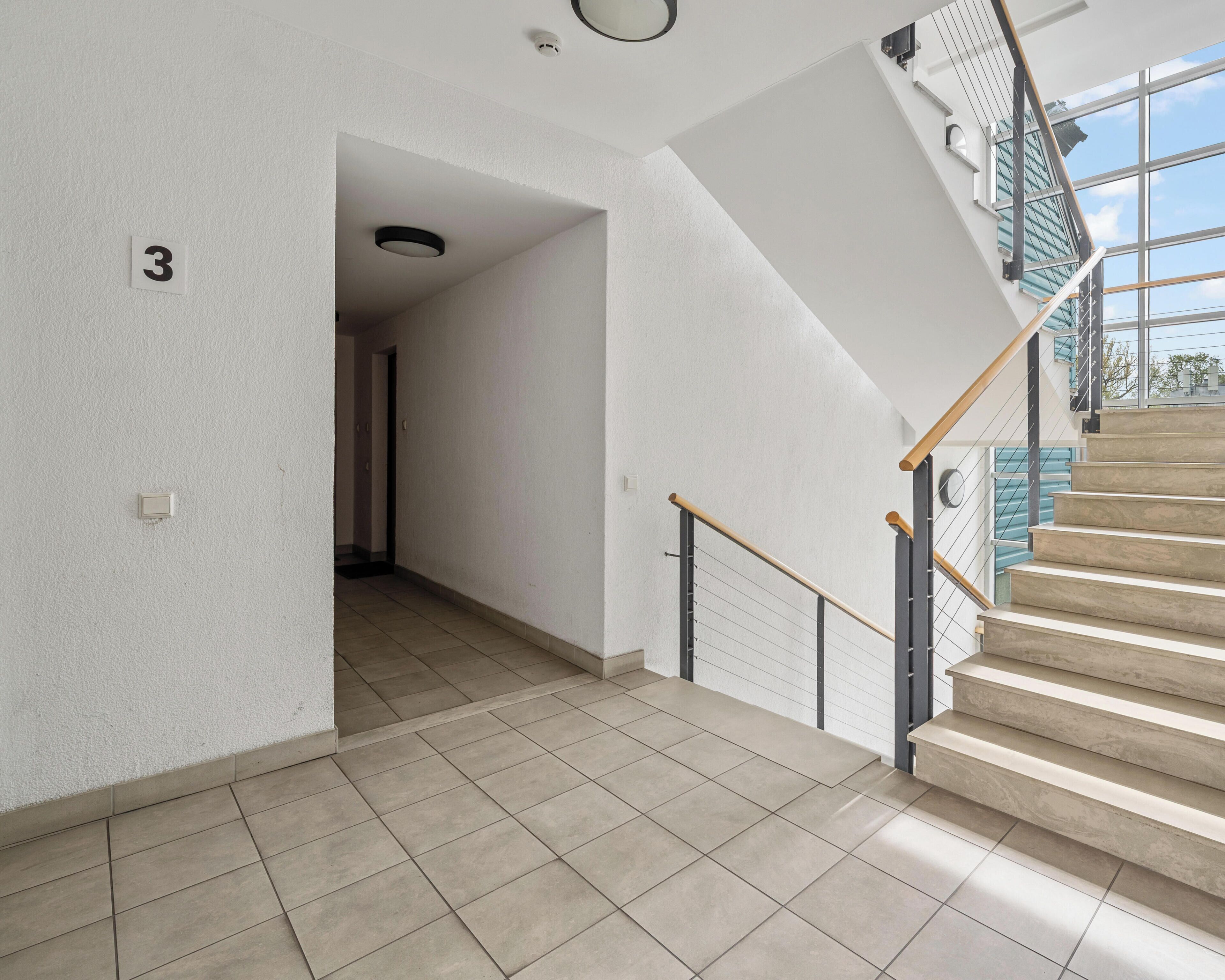 A modern interior with a staircase, tiled flooring, and a visible door with the number 3.