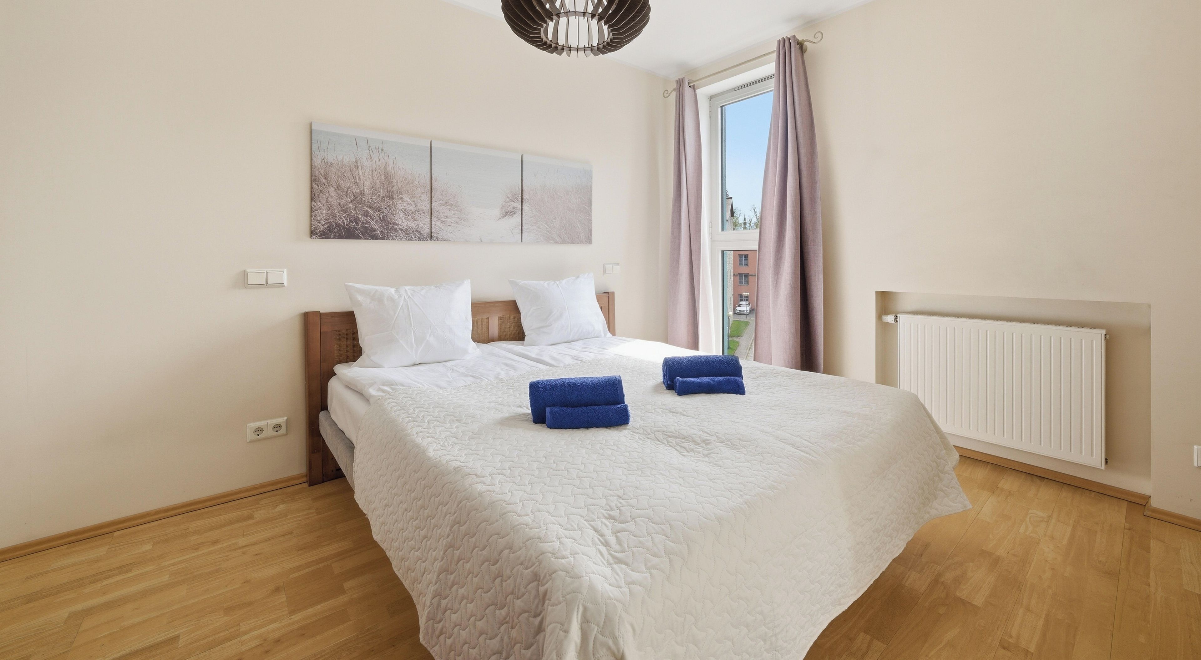 Ein Hotelzimmer mit Bett, einem Fenster mit Vorhängen, einem Heizkörper und einer Wandleuchte.