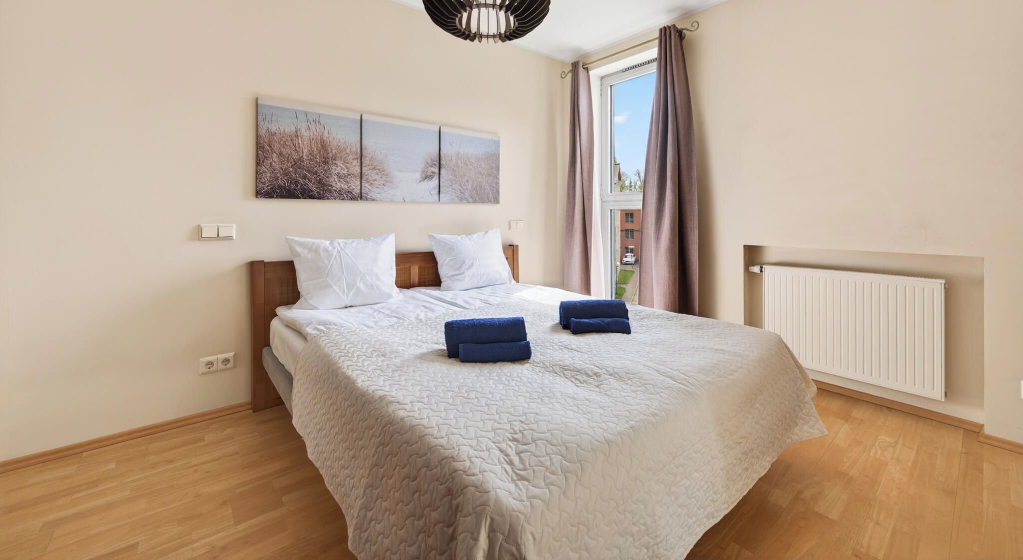 A bedroom with a bed, two pillows, a blanket, a radiator, and a window with curtains.