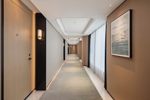 Un pasillo de hotel con piso alfombrado, puertas a ambos lados y una obra de arte enmarcada en la pared derecha.