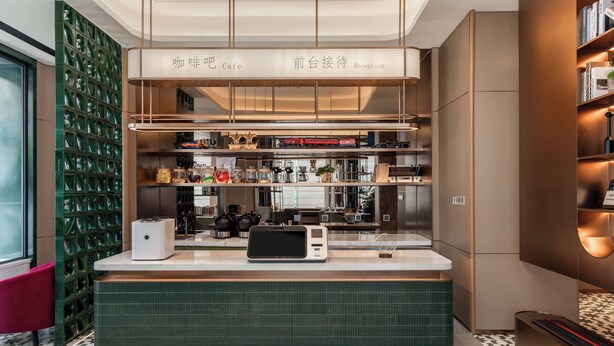 A reception area with a counter, shelves with various items, and a green wall with a unique pattern. - Wanda Yue Wuyi Ancient City (Jinhua)
