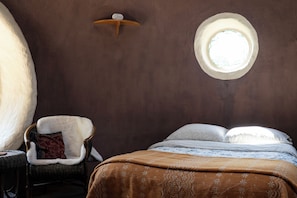 A cozy room with a round window, a wicker chair with a cushion, and a bed with a patterned blanket.