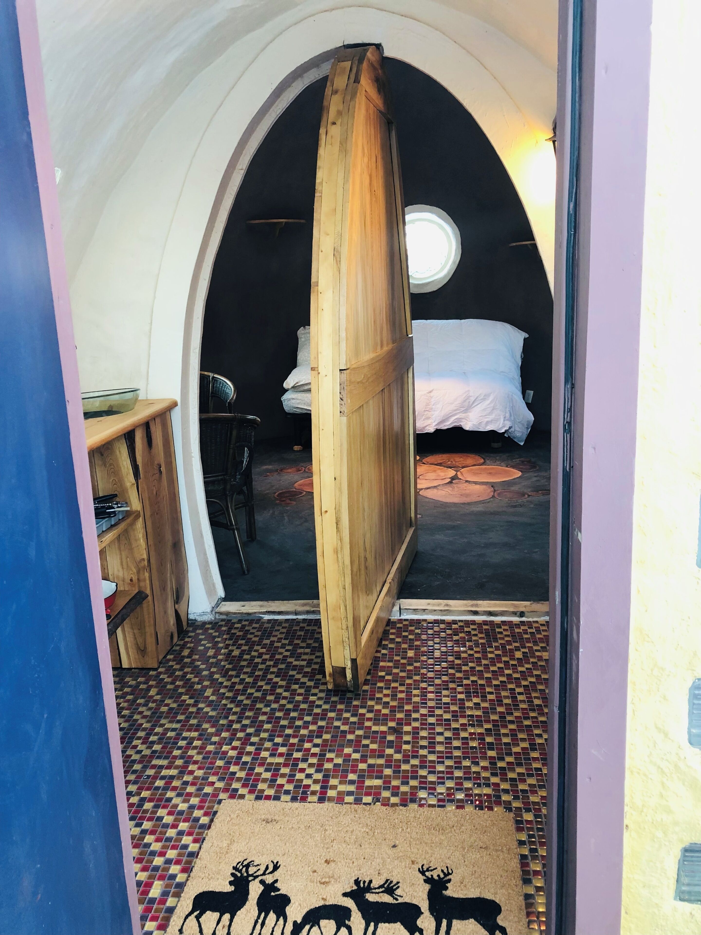 A cozy, arched room with a bed, a wooden door, and a small desk with a chair.