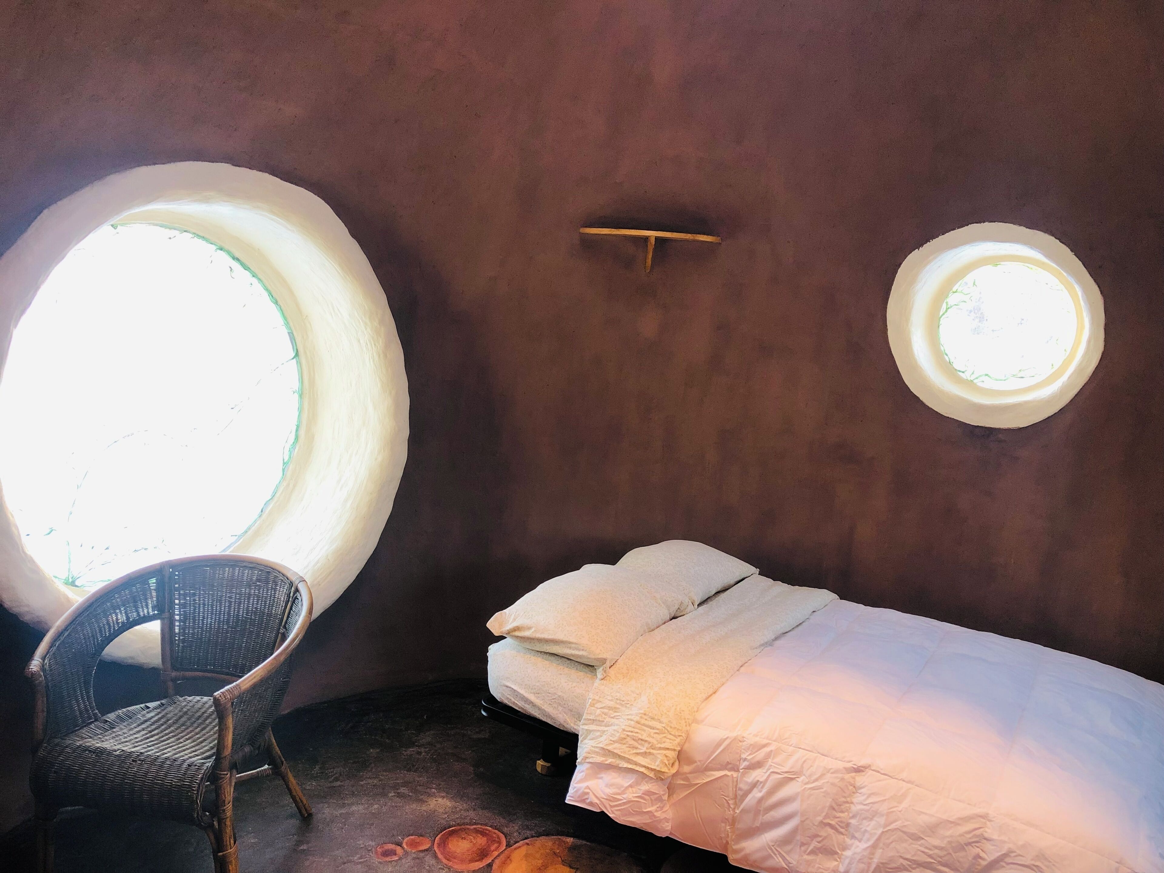 A room with a single bed, a chair, and two circular windows.