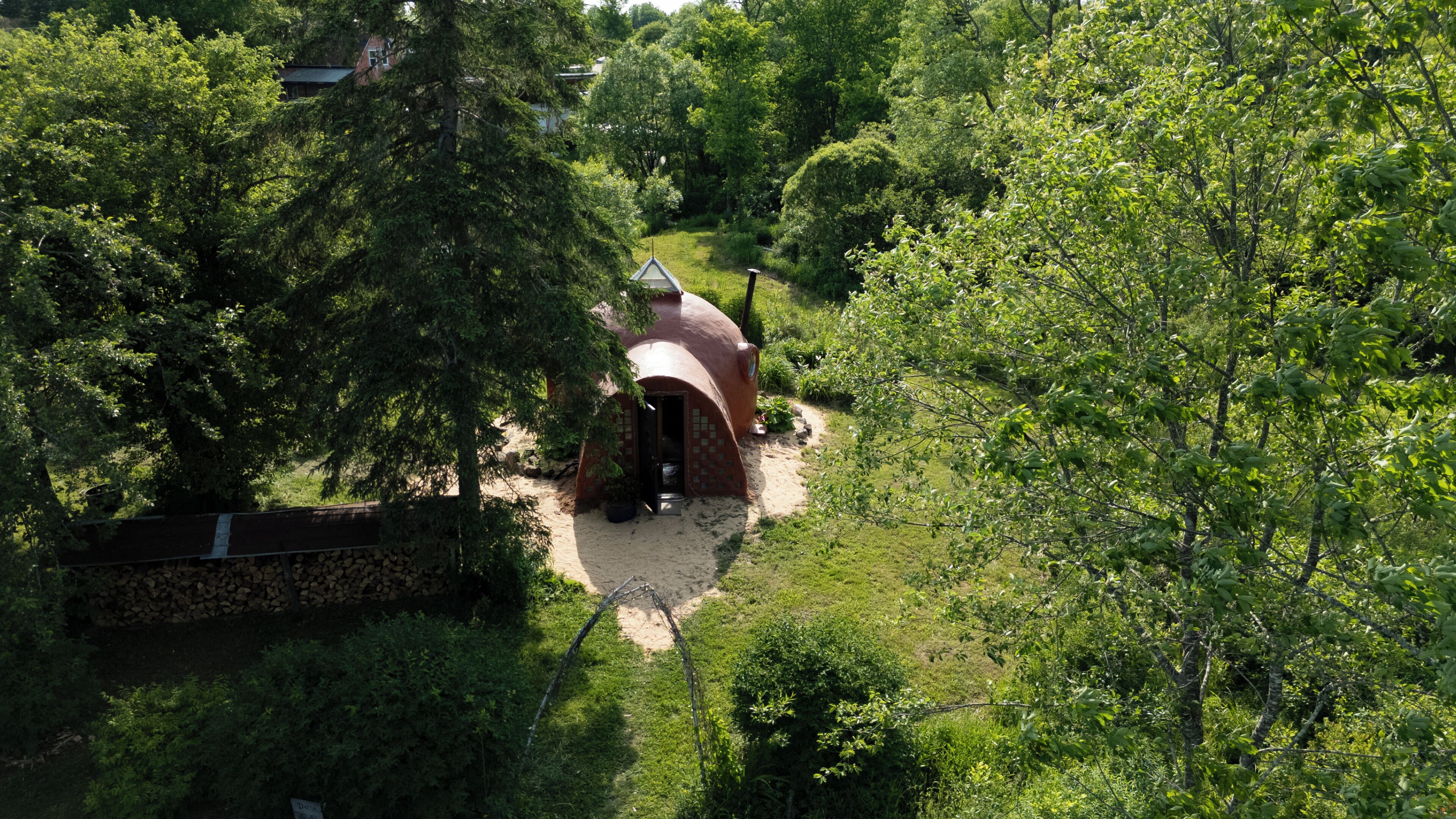 Un bâtiment rustique surmonté d’un dôme, entouré d’une végétation luxuriante et d’un mur de pierre.