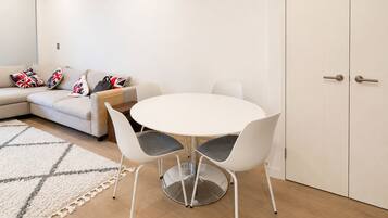 A modern living room with a round white table, two white chairs, a beige sofa with patterned cushions, and a white door.