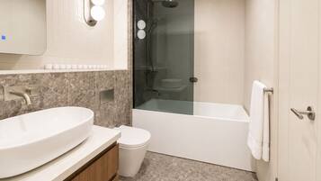 A modern bathroom with a large white sink, a toilet, and a glass-enclosed shower.