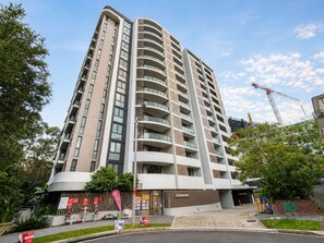 A multi-story hotel with a curved facade, balconies, and a gated entrance. - Modern 2BDR Retreat walk to Metro and Macquarie (Macquarie Park)
