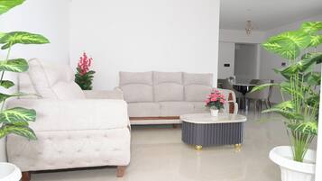 A modern living room with a beige sofa, a round coffee table, and large green plants.