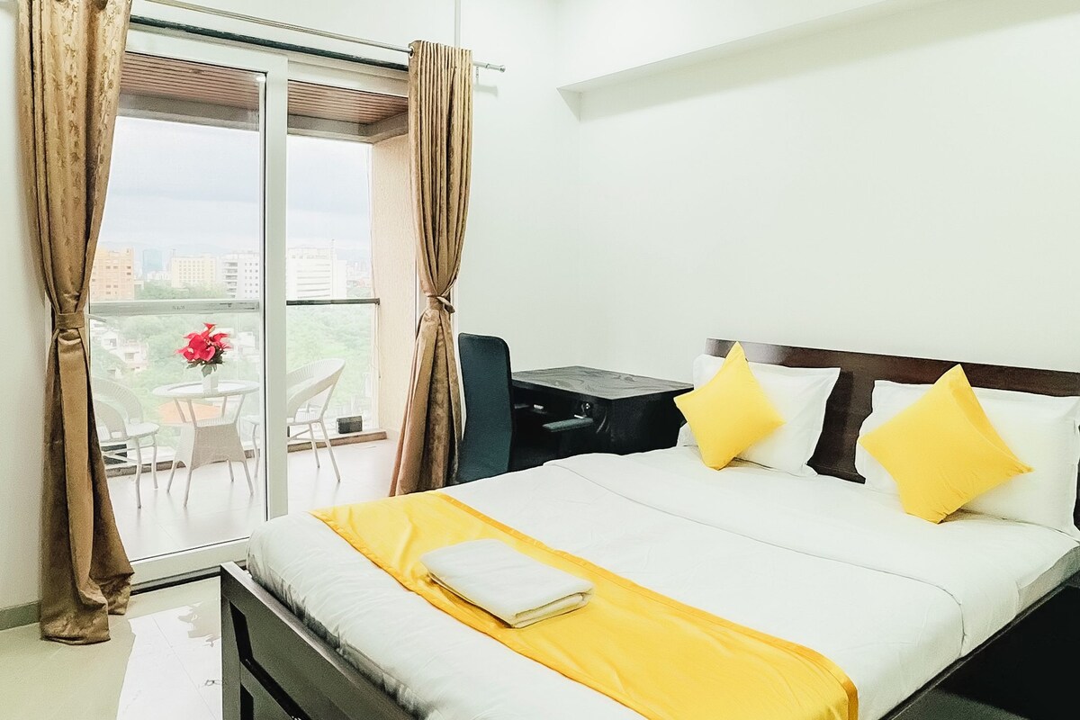 A hotel room with a bed, a table, chairs, a window with curtains, and a ceiling fan.