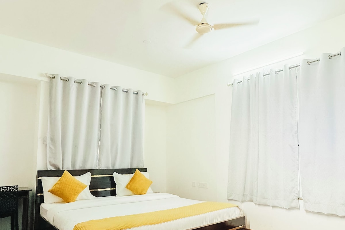 A bedroom with a bed, curtains, a ceiling fan, and a wooden floor.