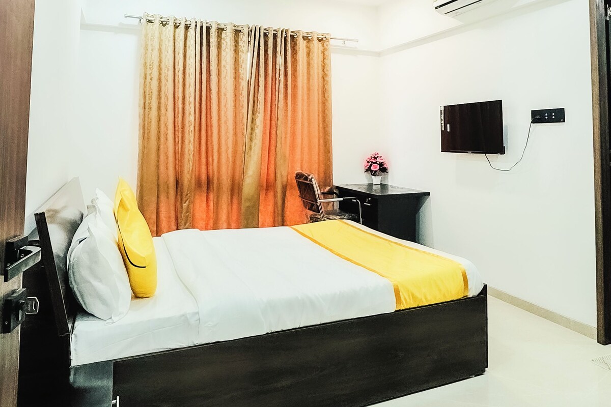 A modern bedroom with a bed, curtains, a desk, a chair, and a television.