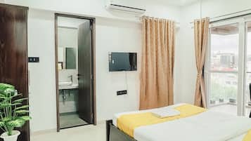 Habitación de hotel con cama, televisor, aire acondicionado, baño y vista al exterior.