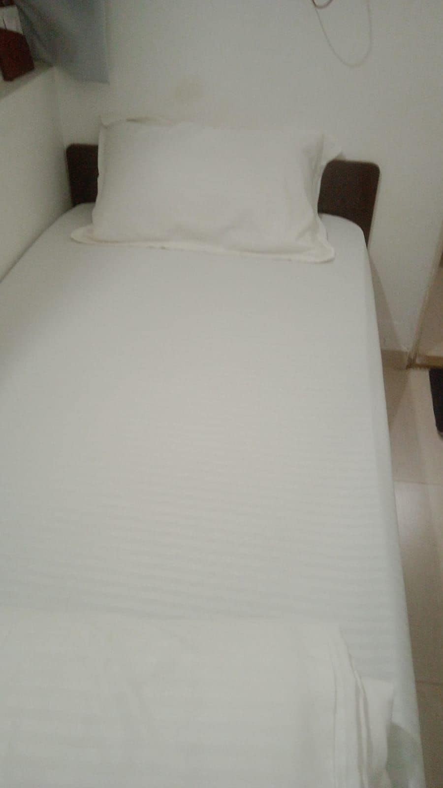A bed with white bedding, wooden headboard, and a wall-mounted light fixture.