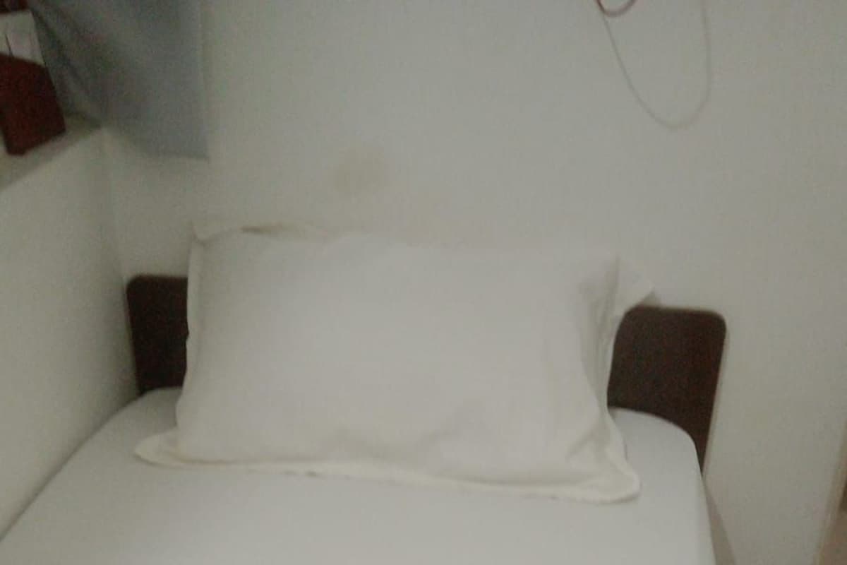 A bed with white bedding, wooden headboard, and a wall-mounted light fixture.