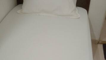 A bed with white bedding, wooden headboard, and a wall-mounted light fixture.