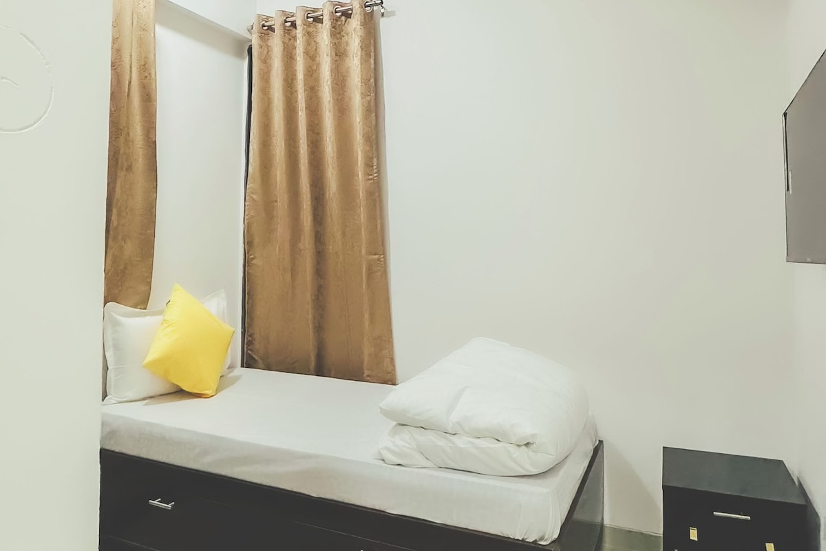 A bedroom with a bed, curtains, a ceiling fan, and a small black cabinet.