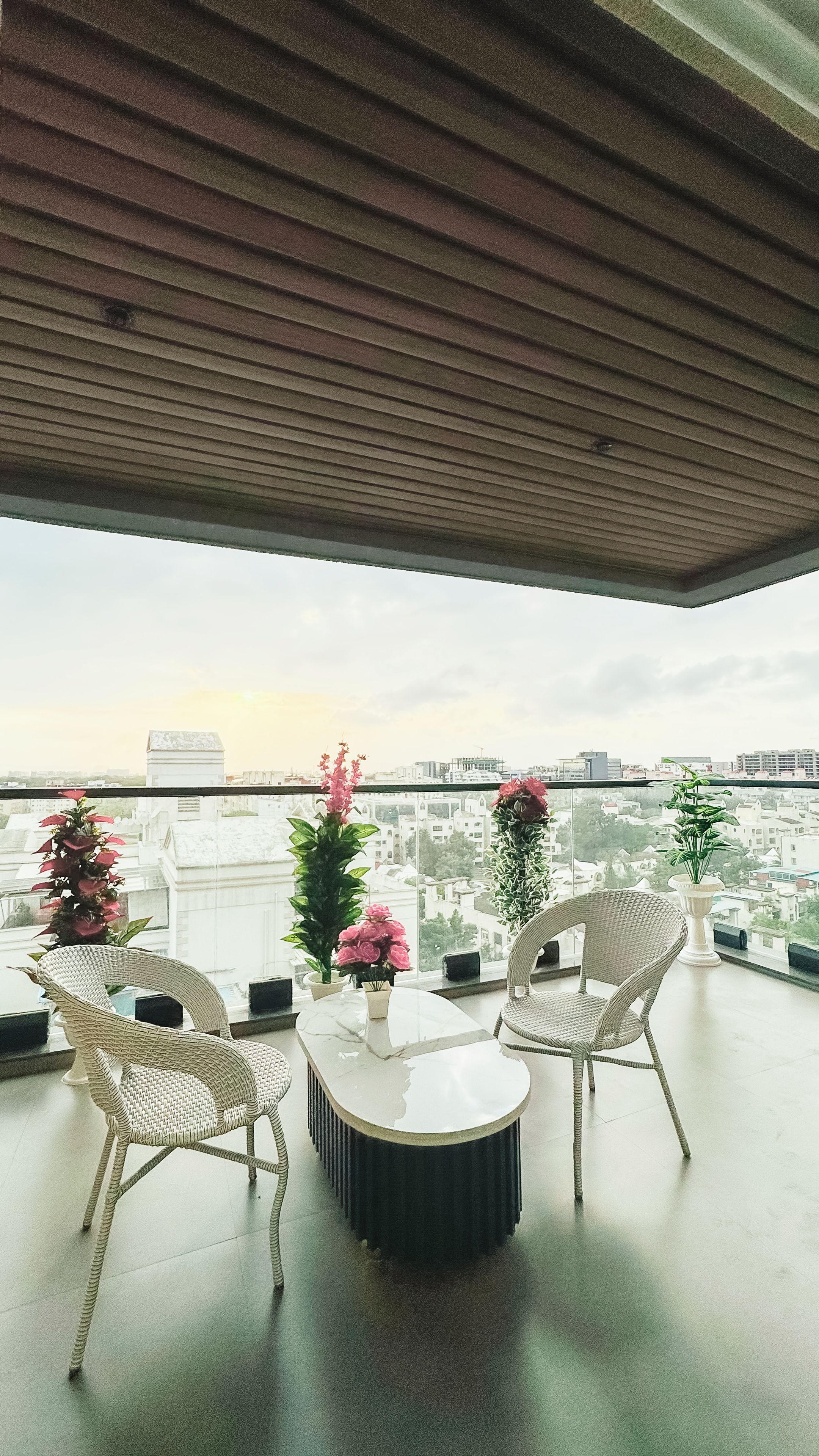 Un balcon avec des fauteuils en osier, une table ronde et des plantes en pot.