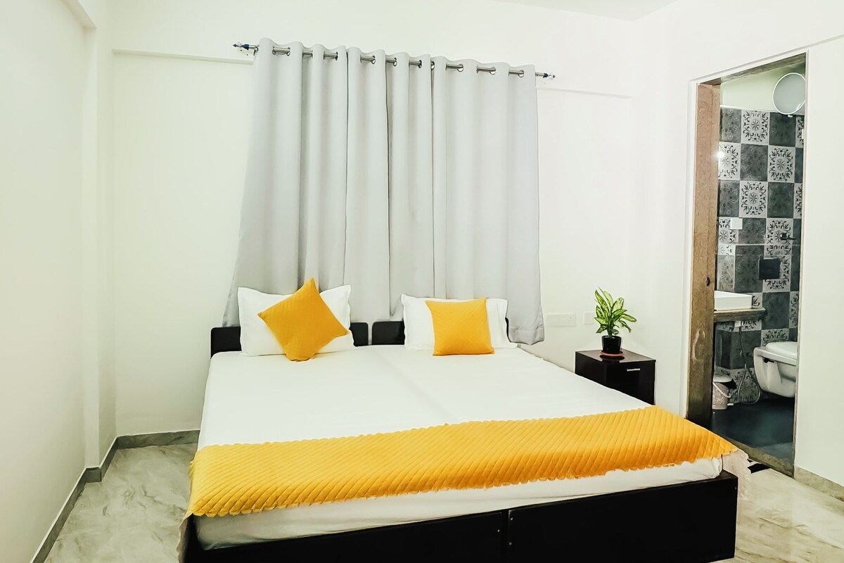 A modern bedroom with a bed, curtains, a ceiling fan, and a bathroom visible through an open door.