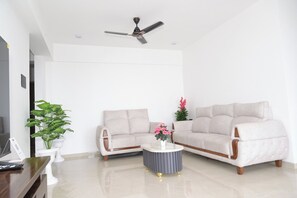 A modern living room with two sofas, a coffee table, a ceiling fan, and a potted plant. - Hotel Nestoria Corporate Services Aparts (Pune)