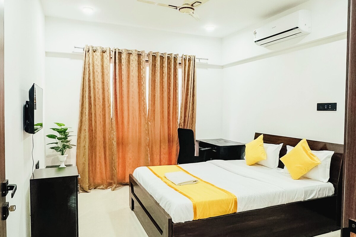 A hotel room with a bed, bedside table, a ceiling fan, an air conditioning unit, and a television on the wall.