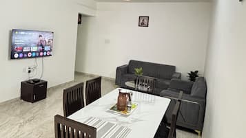 Un comedor con una mesa y sillas, un sofá, un televisor montado en la pared y un ventilador de techo.