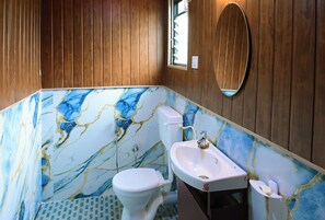 Un baño con pared de mármol, paneles de madera, un inodoro, un lavabo y un espejo.