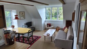 Una sala de estar acogedora con una mesa de comedor, un sofá, un televisor y una ventana con vistas a zonas verdes.