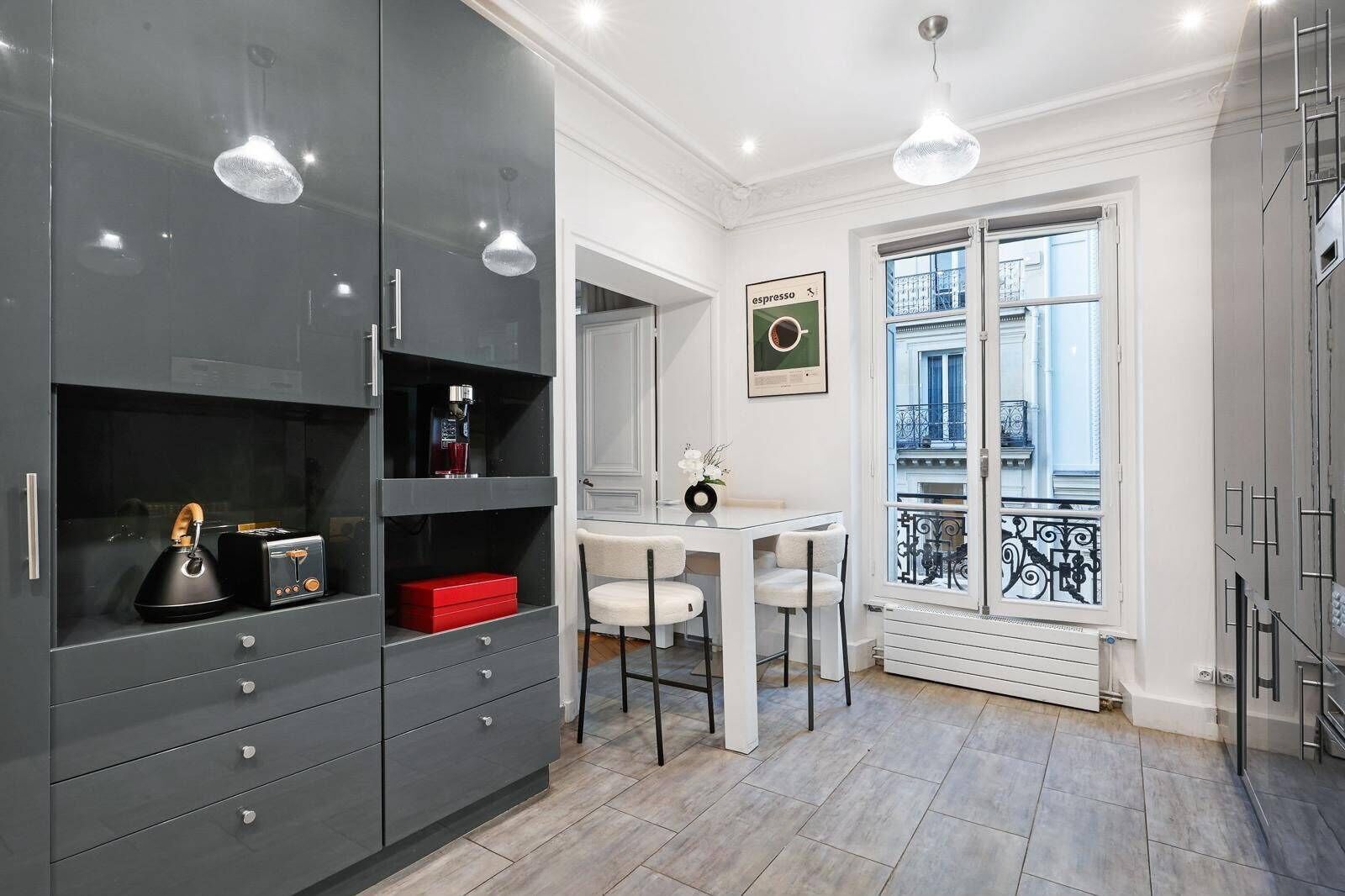A modern kitchen with grey cabinets, a white dining table, and a balcony with a wrought iron railing.