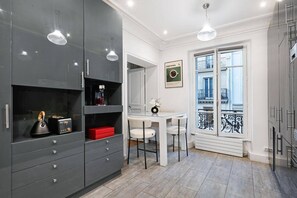Eine moderne Küche mit grauen Schränken, einem weißen Esstisch und einem Balkon mit schmiedeeisernem Geländer.