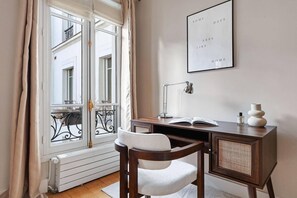 A room with a desk, chair, radiator, window with curtains, and a framed quote on the wall. - Luxury Three-Bedroom Apartment near Parc Monceau – Paris 8th (Paris)