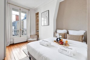 A hotel room with a bed, a chair, a balcony, and a view of buildings. - Luxury Three-Bedroom Apartment near Parc Monceau – Paris 8th (Paris)